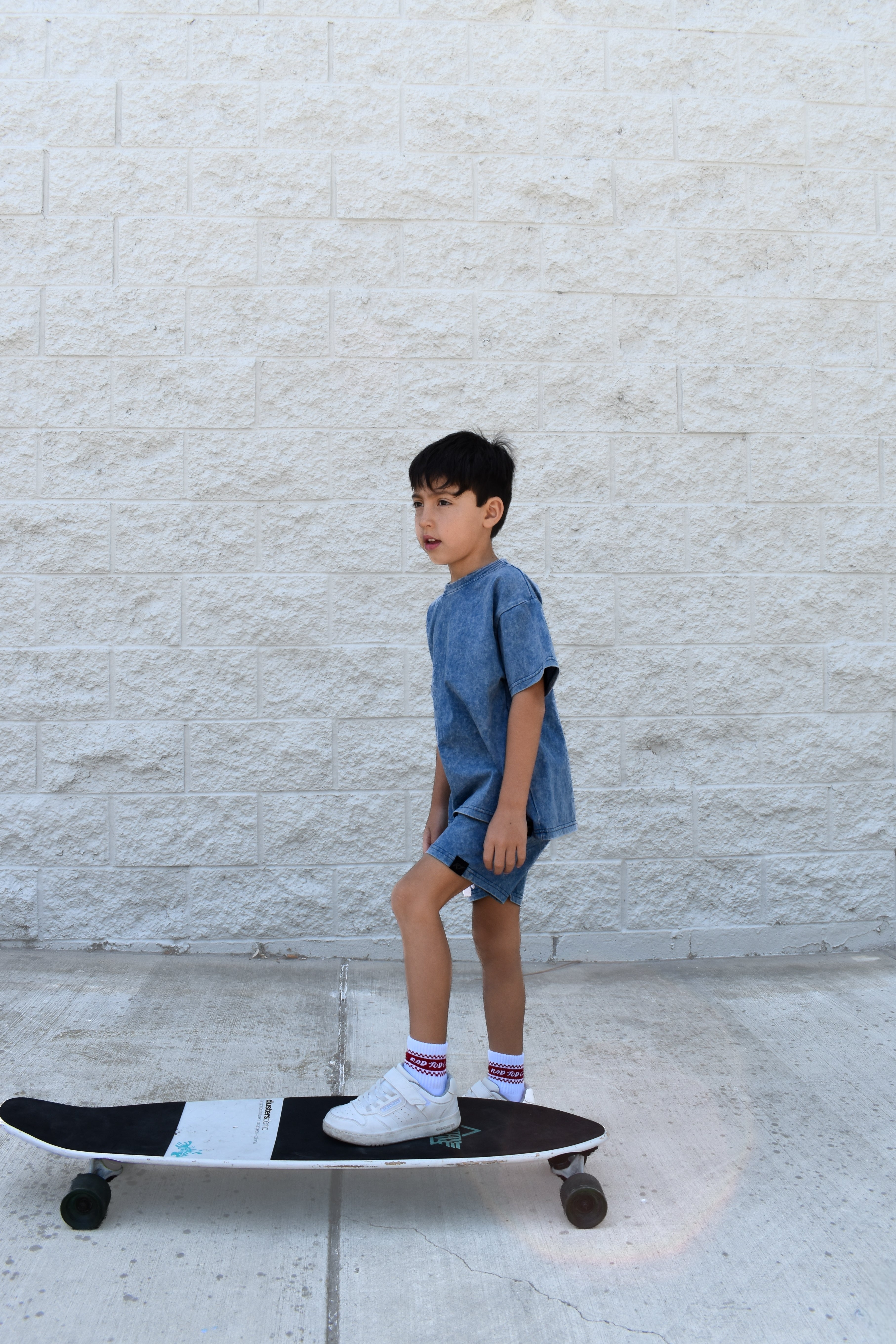 Child standing on a skateboard against a light-colored wall wearing vintage blue set