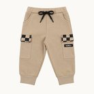 A pair of beige jogger-style cargo pants with a black drawstring, side pockets, and flap cargo pockets featuring a black-and-beige checkerboard pattern. A small black brand patch on the right pocket reads 'rad tod co'.