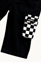 Close-up of black denim pants with a flap pocket featuring a black and white checkerboard pattern and a visible 'Rad Tod Co.' logo patch.