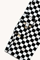 A close-up of a black and white checkered fabric accessory with a flap closure and metal snap hardware, photographed on a plain light background.