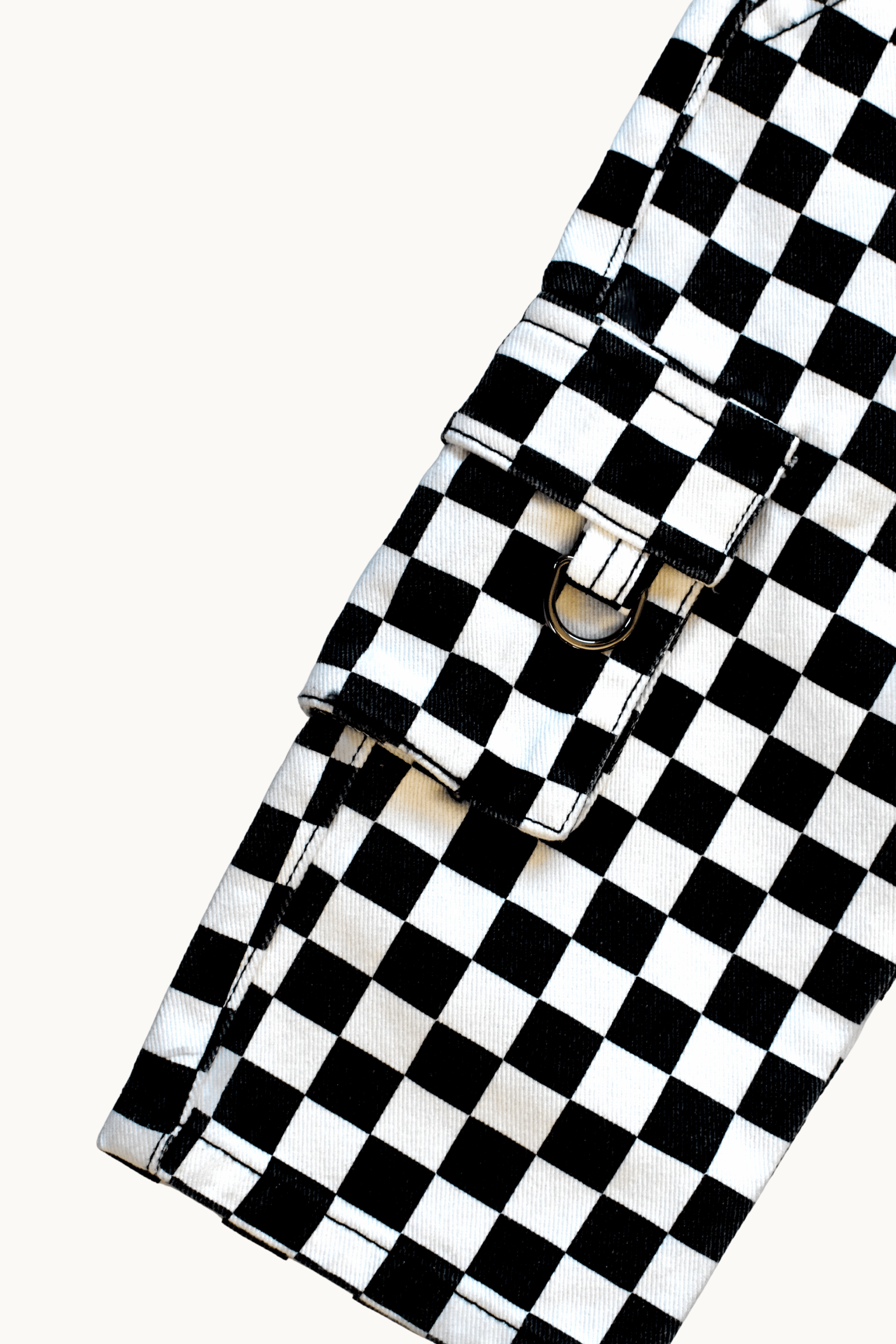 A close-up of a black and white checkered fabric accessory with a flap closure and metal snap hardware, photographed on a plain light background.