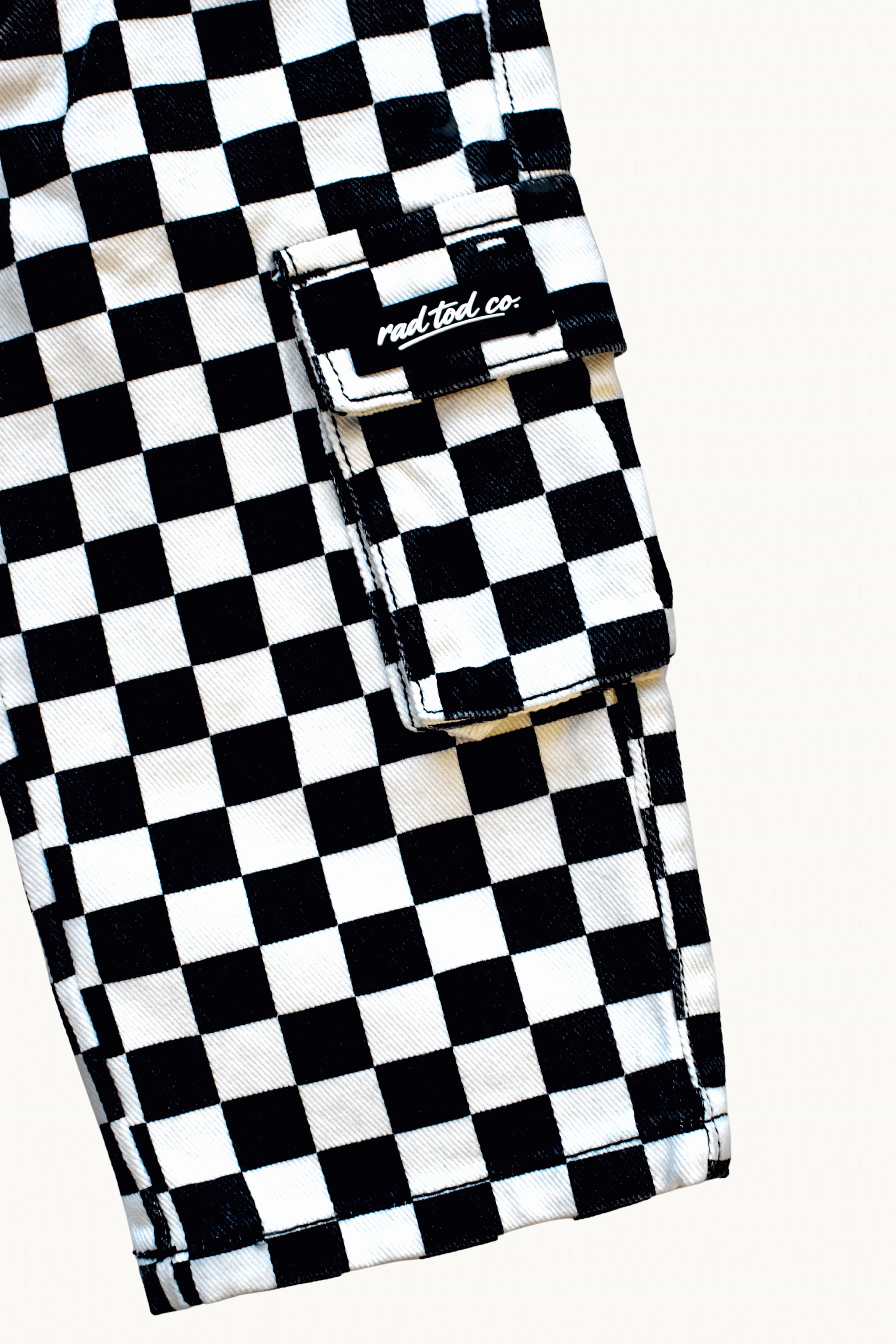 Close-up of a black and white checkered cargo pocket with a flap and a visible 'Rad Tod CO.' label, on a light off-white background.