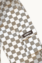 Close-up of a checkered cargo pocket in a brown and white checkerboard pattern, featuring a black brand patch that reads 'Rad Tod co.' on a light off-white background.