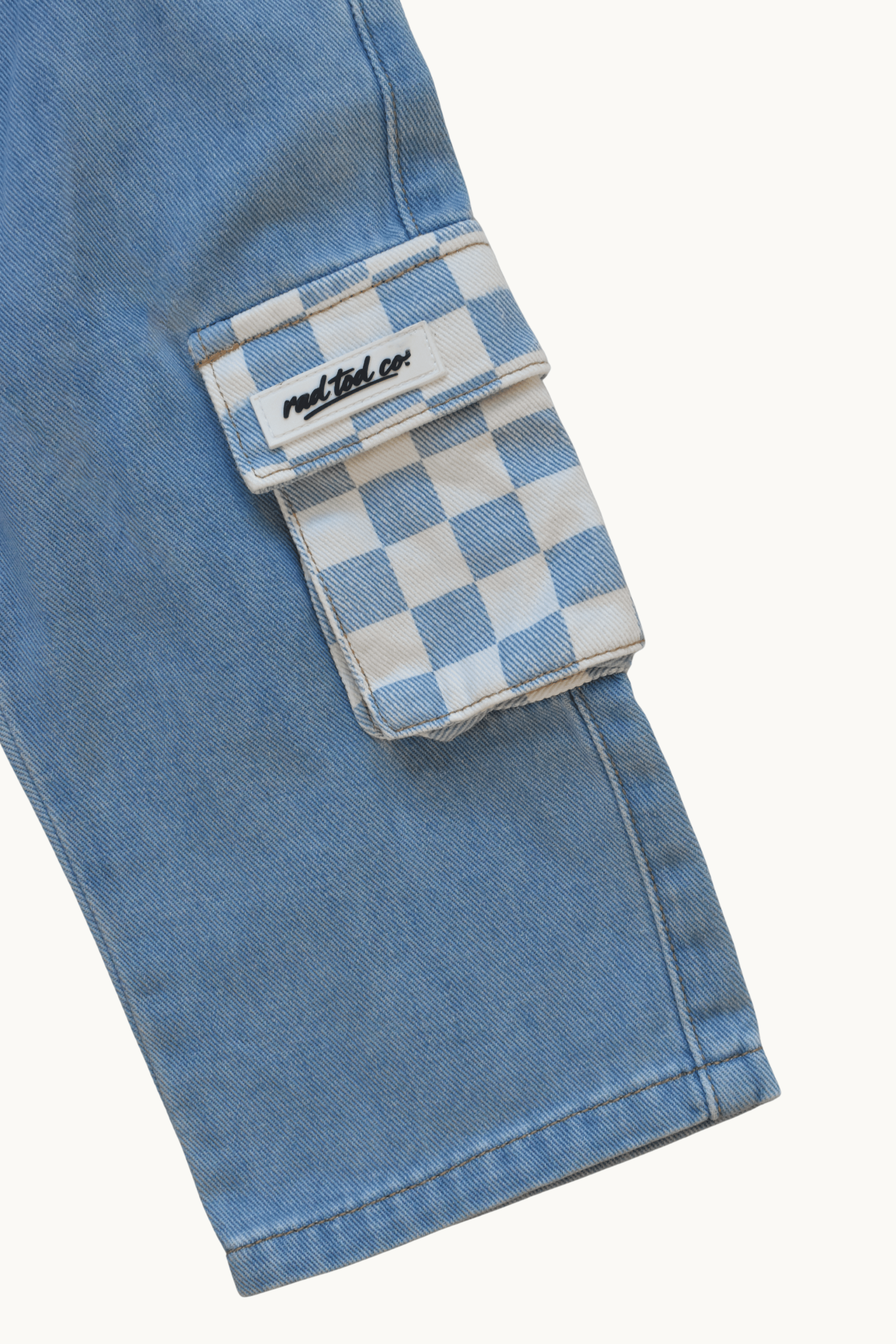 Close-up of a light blue denim cargo pocket with a blue and white checkerboard flap and a visible 'Rad Tod Co.' label.